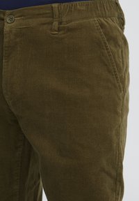 Pantalone od kordura maslinasto zelene boje s teksturiranom površinom, bočnim džepovima i prednjim zatvaranjem na dugme. Prilago�đeni kroj s pojasom.
