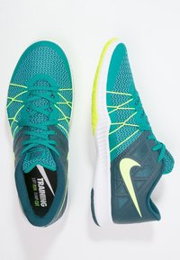 Zapatillas de entrenamiento turquesa con parte superior de malla texturizada, acentos en verde lima y un talón gris reforzado. Presenta suela blanca de goma y cordones.