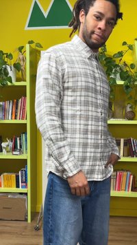 Camicia a quadri con bottoni nei toni del beige chiaro, grigio e blu; maniche lunghe con polsini con bottoni. Indossata con pantaloncini di denim blu.