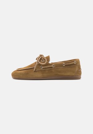 Brown suede moccasin shoe featuring a round toe, decorative lacing with metal eyelets, and a flat rubber sole. Smooth texture and casual design.