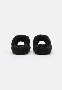 Paire de chaussons noirs duveteux à dos ouvert avec semelles épaisses rembourrées, présentée de face sur fond blanc uni.