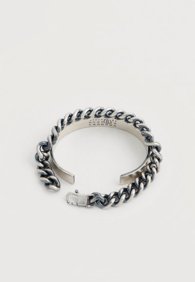 Ασημένιο χοντρό βραχιόλι αλυσίδας με ανοικτή μάνικα και κούμπωμα στυλ αστακού, με μικρούς τυπωμένους αριθμούς στο εσωτερικό της μπάντας.