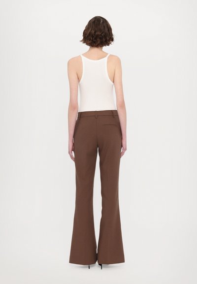 Pantalons marron évasés avec une texture lisse et une poche arrière, associés à un débardeur blanc ajusté. Vue arrière sur fond uni.