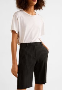 Shorts noirs à rayures avec une coupe ajustée, dotés de poches latérales et d'une texture lisse. Associés à un t-shirt rose clair à coupe décontractée.