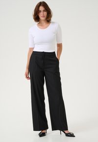 Pantaloni negri cu picioare late și talie cu șnur, asortați cu un top alb ajustat cu mânecă scurtă. Textură de țesătură netedă și design structurat.