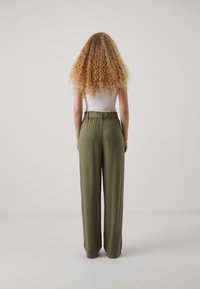 Pantalon vert à jambes larges avec une taille ajustée et un détail de ceinture, réalisé dans un tissu lisse. Associé à un top blanc simple.