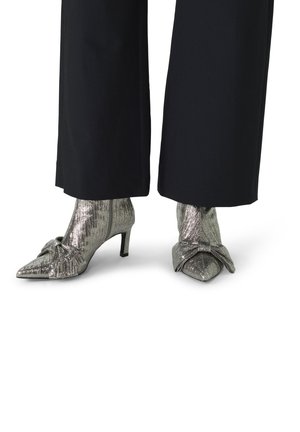 Metallic silver pointed toe heels with a textured finish. Features a small bow detail on the side and a low stiletto heel.