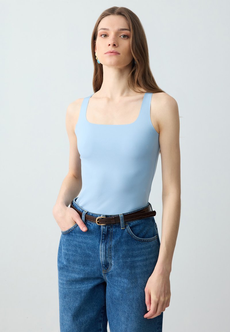 Top senza maniche di colore azzurro chiaro con scollatura quadrata abbinato a jeans in denim blu a vita alta e una cintura marrone con fibbia dorata.