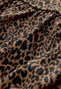 Leopardenmusterstoff in verschiedenen Brauntönen und Schwarz, mit einer strukturierten Oberfläche, die aufwendige Muster und unterschiedliche Fleckengrößen aufweist.