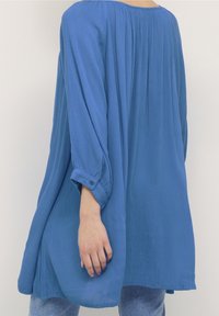 Blusa lunga e morbida a maniche lunghe di un blu vivace. Realizzata in tessuto testurizzato con scollatura rotonda e polsini con bottoni. Presenta delle pieghe sul retro.