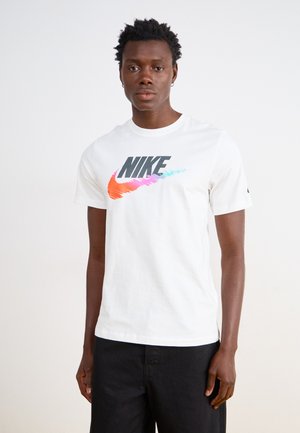 Hvid bomulds-T-shirt med et fremtrædende sort "NIKE" logo med farverige gradient detaljer i orange, pink og teal. Korte ærmer; rund hals.