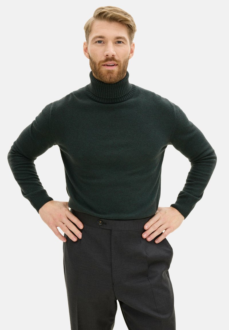 Dunkelgrüner Rollkragensweater aus weichem Material, körpernahe Passform, gerippter Kragen, kombiniert mit maßgeschneiderten dunkelgrauen Hosen.