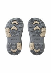 Graue Gummisohle mit strukturierter Oberfläche, die verschiedene geometrische Muster und hellfarbige Akzentstücke zeigt. Logo "reima" sichtbar.