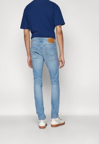 Sovitut vaaleansiniset farkut, joissa on ruskea nahkapaluu, kaksi takataskua ja sileä pinta, yhdistetty tummansiniseen t-paitaan ja valkoisiin tennareihin.