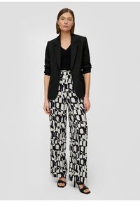 Blazer noir, top noir à col en V, et pantalon large avec un motif géométrique noir et blanc. Comprend des talons hauts et des textures lisses.