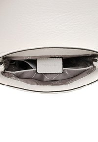 Interno di una borsa in pelle bianca con rivestimento grigio chiaro, dotata di una tasca e di un'etichetta in rilievo con la scritta "Tamaris". Dettaglio della superficie testurizzata visibile.