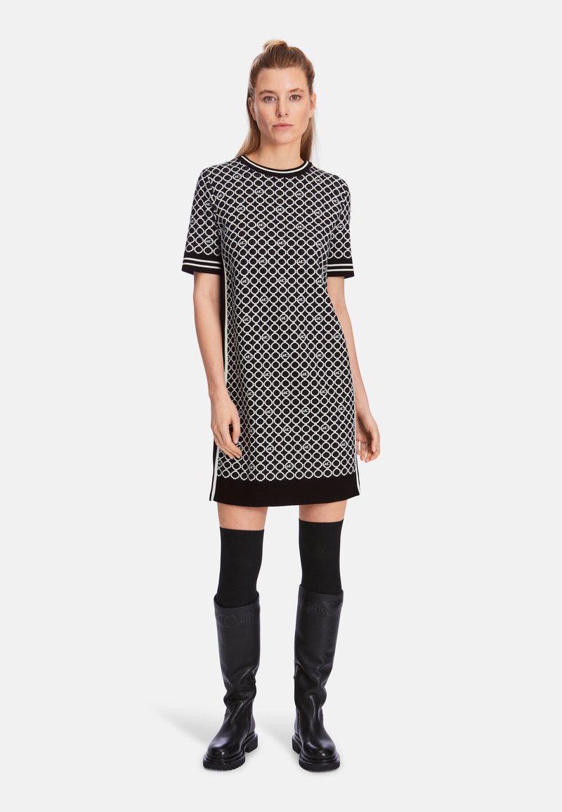 Schwarz-weiß gemustertes kurzärmeliges Kleid mit Rundhalsausschnitt und kontrastierendem schwarzen Saum; kombiniert mit kniehohen schwarzen Stiefeln.