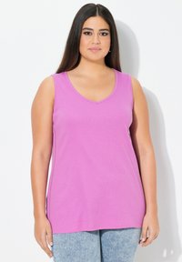 Top senza maniche a V in un brillante colore rosa, realizzato in morbido cotone. Caratterizzato da una vestibilità rilassata e da una sottile cucitura laterale. Abbinato a pantaloni in denim chiaro.