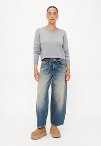 Harmaa lyhyempi huppari, löysät siniset farkut, joissa on naru, ja beige korkea kenkä. Silkkinen kangas, jossa on haalistunut farkkutekstuuri.