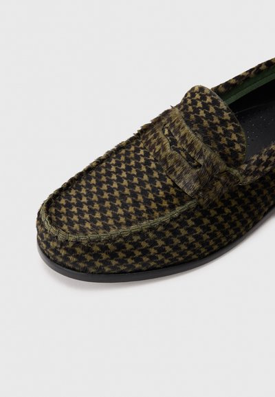 Mocasines para hombre de slip-on con un patrón de espiga en tonos verde oliva y negro, parte superior de tela texturizada, suela negra y detalles cosidos.