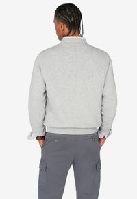 Sudadera de felpa gris con cuello redondeado, puños y cinturilla acanalados. Combinada con pantalones cargo grises que tienen bolsillos laterales.