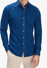 Camicia in denim blu con maniche lunghe, chiusura frontale con bottoni e colletto classico. Presenta una texture liscia e bottoni bianchi a contrasto.