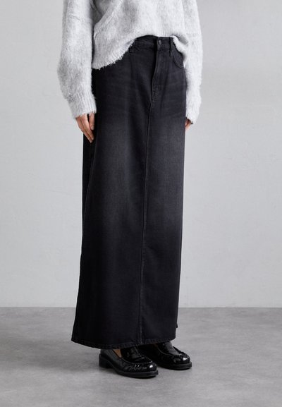Gonna maxi in denim nera con taglio dritto, caratterizzata da vita alta, cuciture a vista e tasche laterali, abbinata a scarpe nere.