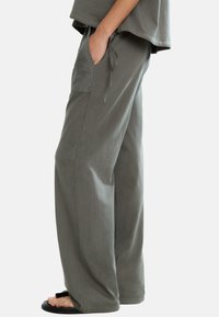 Szare spodnie szerokie z miękkiego materiału, z elastycznym pasem regulowanym na sznurek i bocznymi kieszeniami, z delikatnym kwiatowym wzorem na kieszeni.