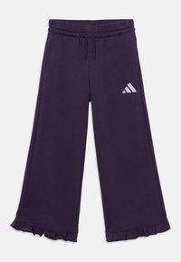 Violeta sporta bikses ar viļņotu apakšmalu un gaišvioletu Adidas logotipu sānos, kas ir izstrādātas komfortam un stilam.
