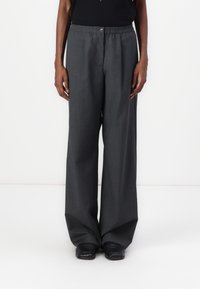Donkergrijze wijde broek met een gestructureerde stof, voorzien van een knoopsluiting en een elastische tailleband. Geselecteerd met zwarte schoenen.