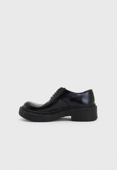 Black leather lace-up shoe with a rounded toe, block sole, and subtle stitching details. Smooth finish with a thick textured sole.