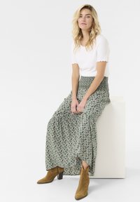 Zelena cvetna maksi krila s nabranim pasom. Bela rebrasta majica s kratkimi rokavi. Rjavi gležnjarji s blok peto.