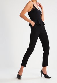 Top peplum negro con detalles de encaje y pantalones negros ajustados. La modelo lleva zapatos de tacón negro. Silueta simple y elegante.