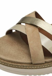 Sandalo in suede beige con cinturini incrociati in crema lucida e oro metallico, caratterizzato da una suola interna testurizzata e una suola leggera e testurizzata.