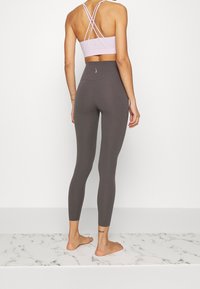Szare legginsy z wysokim stanem i jasnofioletowy stanik sportowy z krzyżowanym plecami, wykonane z gładkiego materiału z minimalnymi szwami oraz niewielkim logo.