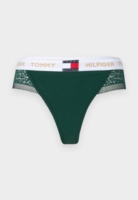 Green cotton thong with lace side accents. Features a white waistband with gold "TOMMY HILFIGER" lettering and logo patch. Smooth texture.