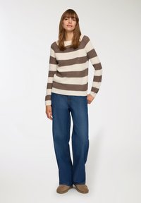 Maglione a righe in beige e marrone, texture lavorata a maglia, maniche larghe, indossato con jeans a gamba larga blu e calzature beige. Design semplice con scollatura rotonda.