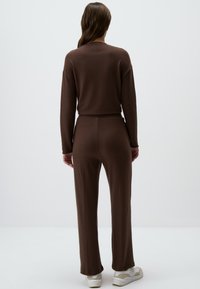 Braunes Strick-Loungewear-Set mit langärmeligem Oberteil und passenden Hosen. Der Stoff ist weich und hat eine lockere Passform. Weiße Sneakers vervollständigen den Look.