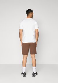 Hvid T-shirt med korte ærmer og brune shorts. T-shirten har en rund halsudskæring; shorts er knælange og lavet af blødt stof. Sorte sneakers og hvide sokker.
