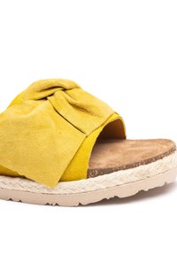 Gelbe Wildledersandale mit einem geknoteten Schleifendetail, weichem Textur, natürlicher Korkfußbett und einer mit Jute umwickelten Sohle für zusätzlichen Kontrast.
