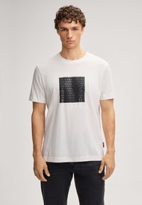 Witte t-shirt met korte mouwen van katoen, met een vierkante graphic in zwart met herhaalde tekst in wit en grijs. Slank gesneden.