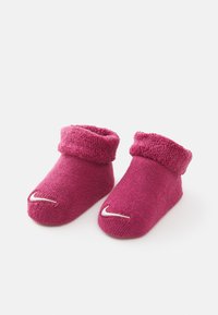 Fuksijaste pletene otroške nogavice s prevratenim robom, z belim logotipom Nike spredaj in odprtim prstom. Mehka tekstura po celotni površini.