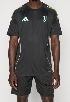 Homme portant un uniforme de football Juventus noir avec des logos bleu clair, des bandes jaunes sur les épaules et des liserés roses sur le maillot et le short.