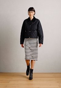 Quilted black cropped jacket with a pointed collar, worn over a knee-length striped black and white skirt, and black ankle boots.