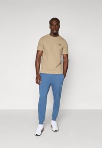 Tan bomull t-shirt med strukturerad yta och liten logotyp; blå joggingbyxor med elastiska muddar; vita sneakers med accenter.