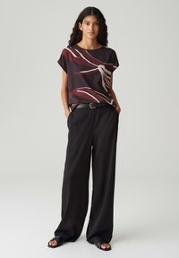 Korte mouwen, donker bordeaux top met abstracte crèmekleurige en rode patronen, gecombineerd met losse zwarte broek en eenvoudige zwarte sandalen.