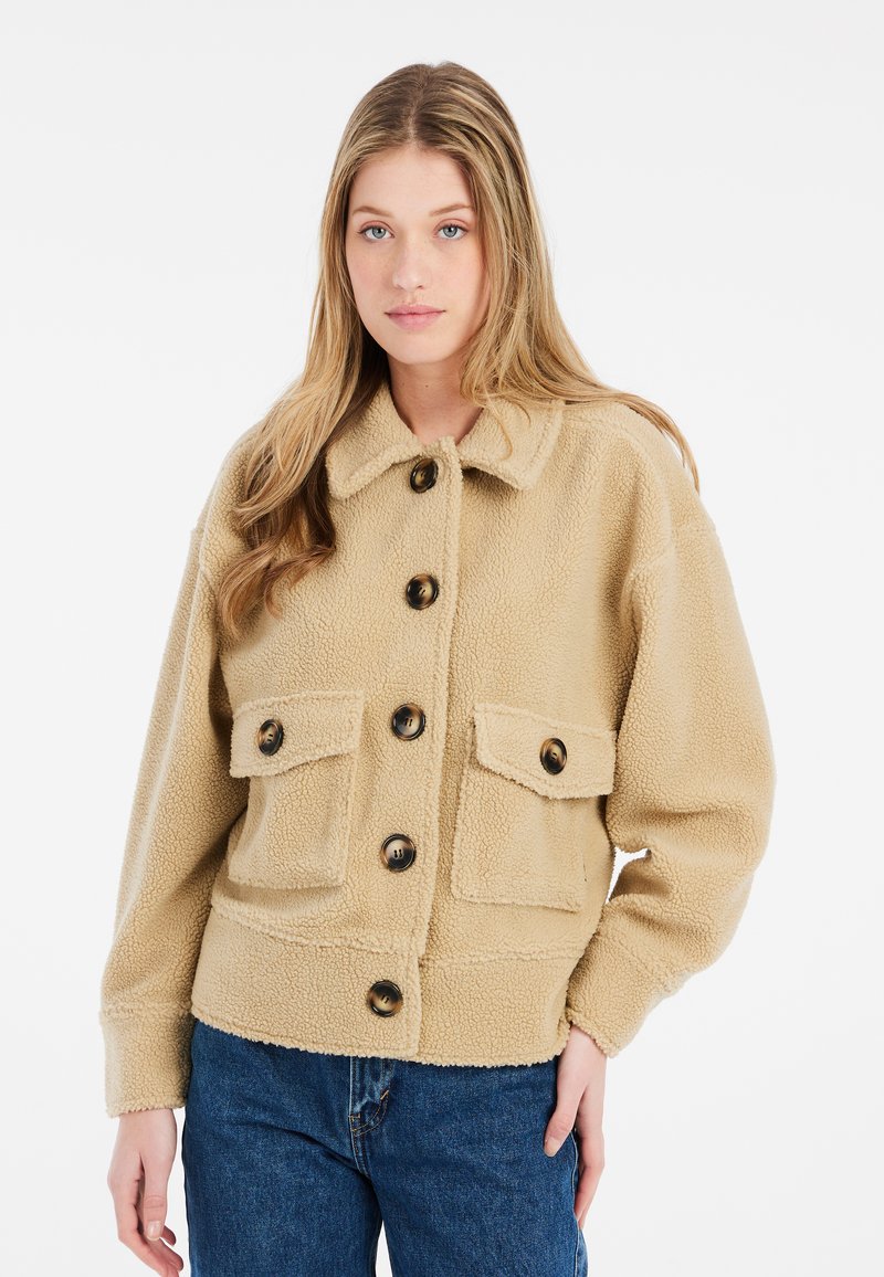 Beige fleece jakke med krave, frontlukning med knapper og to store påsatte lommer med brune knapper.