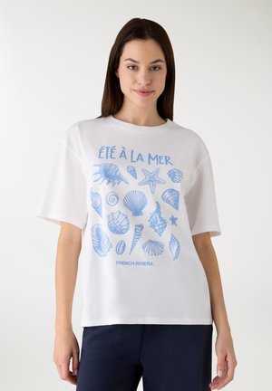 Maglietta bianca con stampa di una conchiglia blu e una stella marina, con i testi "ÉTÉ À LA MER" e "FRENCH RIVIERA" nella parte inferiore. Maniche corte.