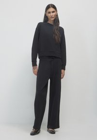 Felpa nera rilassata con maniche lunghe, abbinata a pantaloni neri a gamba larga con vita con cordino, completata da scarpe basse nere con borchie.