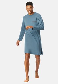 Robe de nuit longue à manches longues bleue avec un col rond et une poche à motif à carreaux. Tissu doux et fentes latérales pour plus de liberté de mouvement.